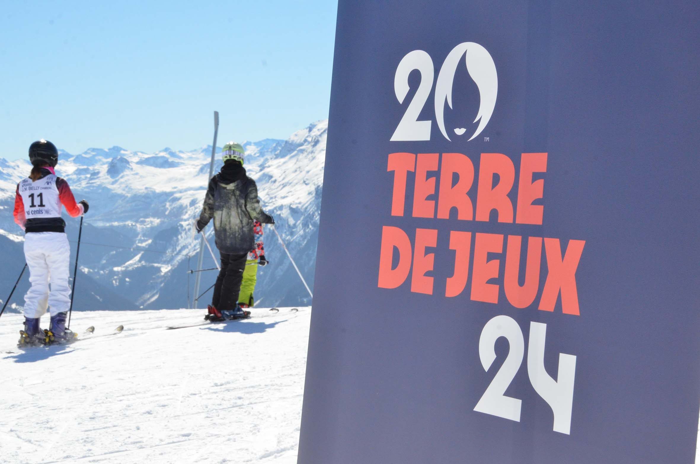deux enfants skieurs de dos et au premier plan l'oriflamme Terre de Jeux 2024